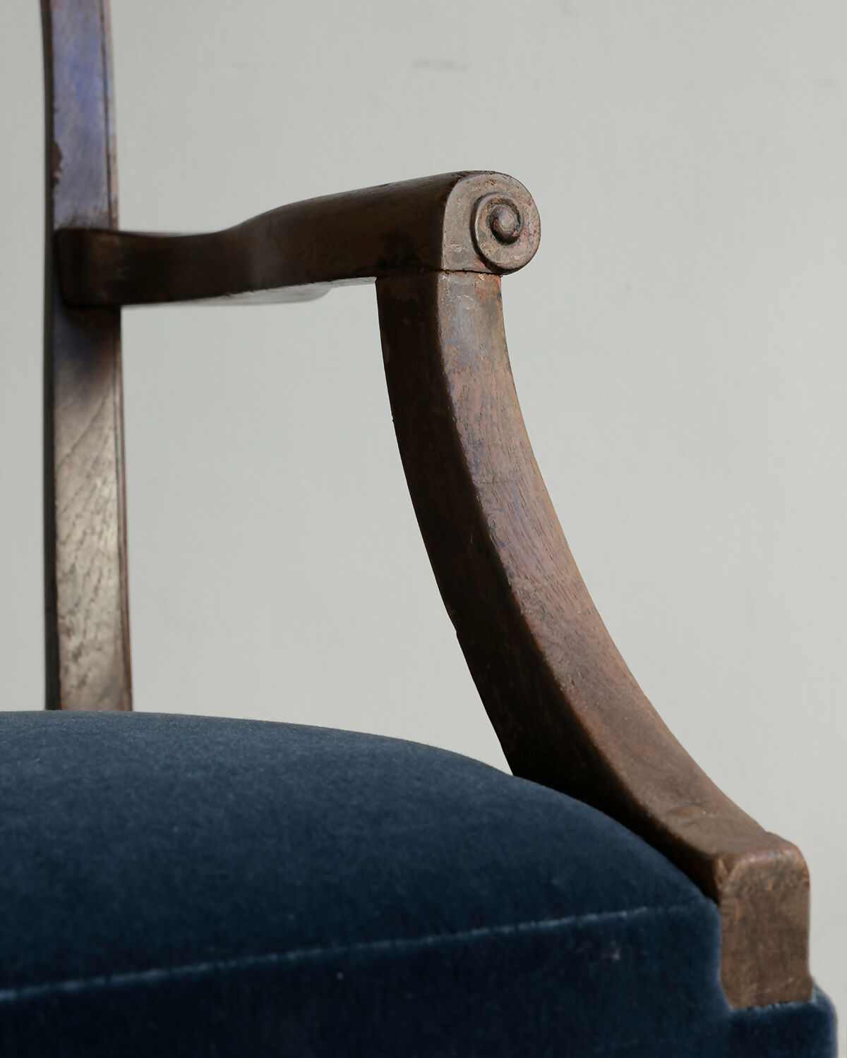 Close-up of a chair arm with wooden armrest and blue cushion against a neutral background,available to buy from the-salon.com. SALON curates the finest unique handmade pieces from the interior industry's best makers and brands. Shop luxury furniture, lighting, rugs, art, antiques and vintage pieces and accessories from SALON interior designed rooms. 