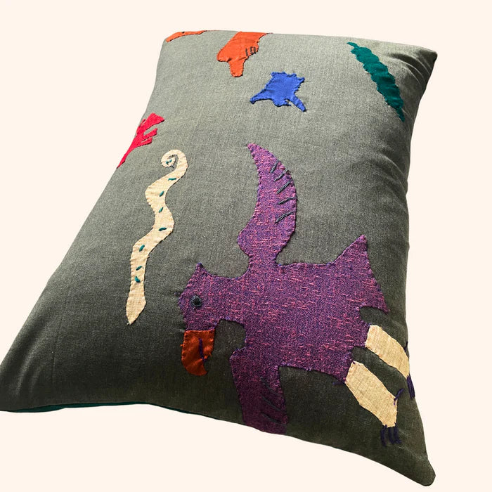A rectangular cushion with a geometric pattern featuring abstract characters in various colors on a gray background,  available  to buy on the-salon.com. SALON curates the finest , unique, handmade pieces from the interior industry's best makers and brands. Shop luxury furniture, lighting, rugs, art, antiques and vintage pieces and accessories from SALON interior designed rooms.