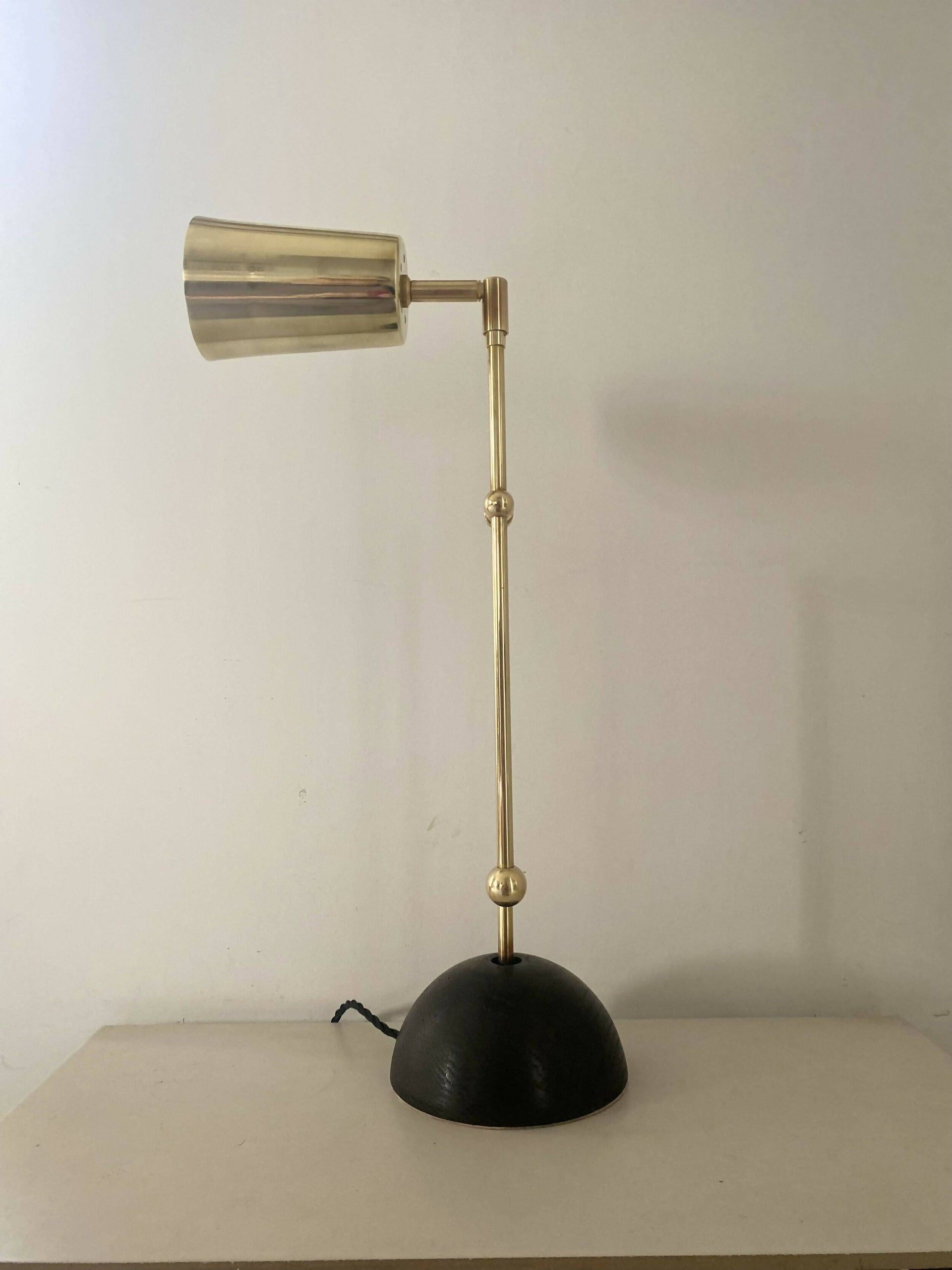 An elegant brass desk lamp with a hand turned solid oak base and a hand polished brass finish, positioned against a neutral background,  available  to buy on the-salon.com. SALON curates the finest , unique, handmade pieces from the interior industry's best makers and brands. Shop luxury furniture, lighting, rugs, art, antiques and vintage pieces and accessories from SALON interior designed rooms.