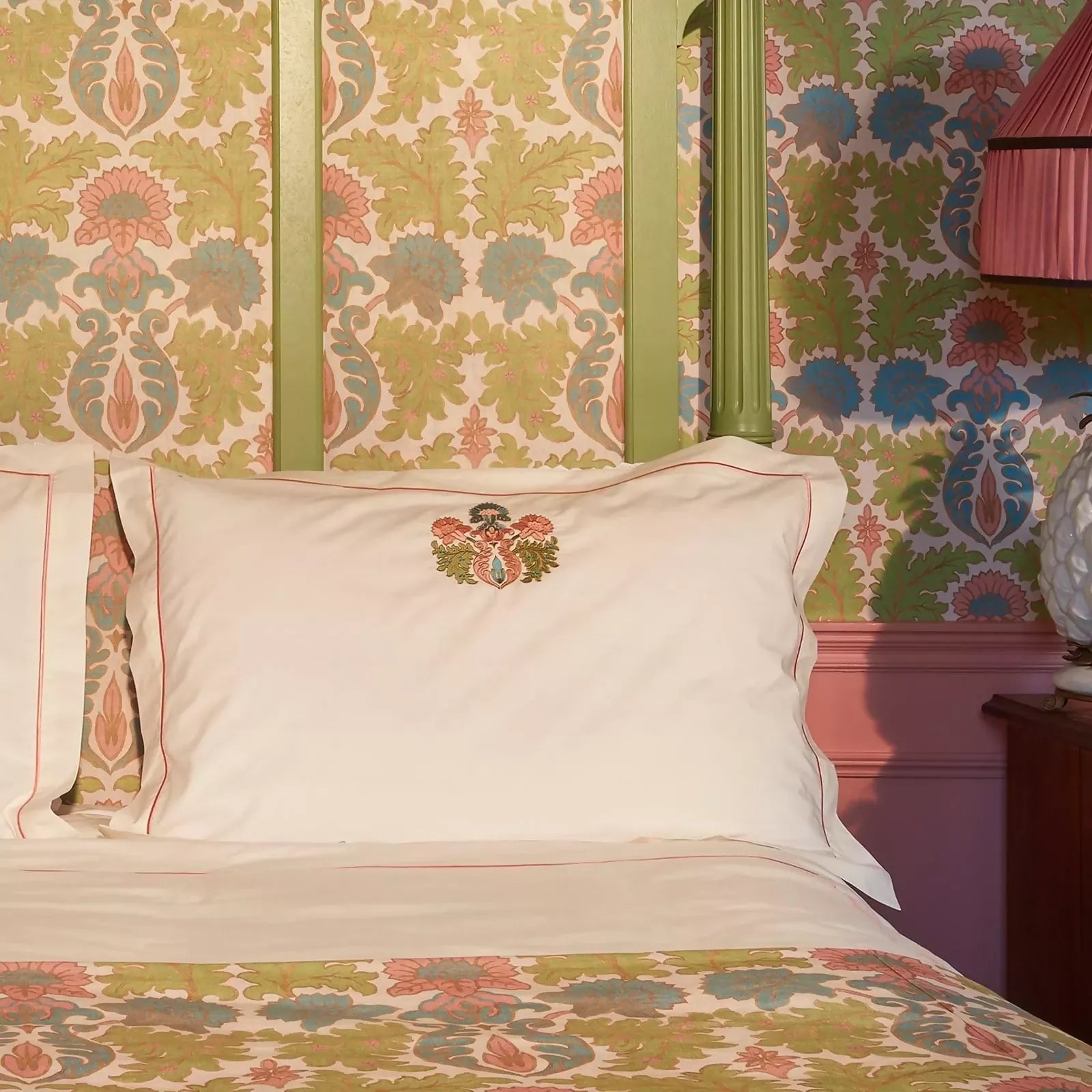 Decorative pillow with a coat of arms on a bed with patterned bedding and wallpaper,  available  to buy on the-salon.com. SALON curates the finest , unique, handmade pieces from the interior industry's best makers and brands. Shop luxury furniture, lighting, rugs, art, antiques and vintage pieces and accessories from SALON interior designed rooms.