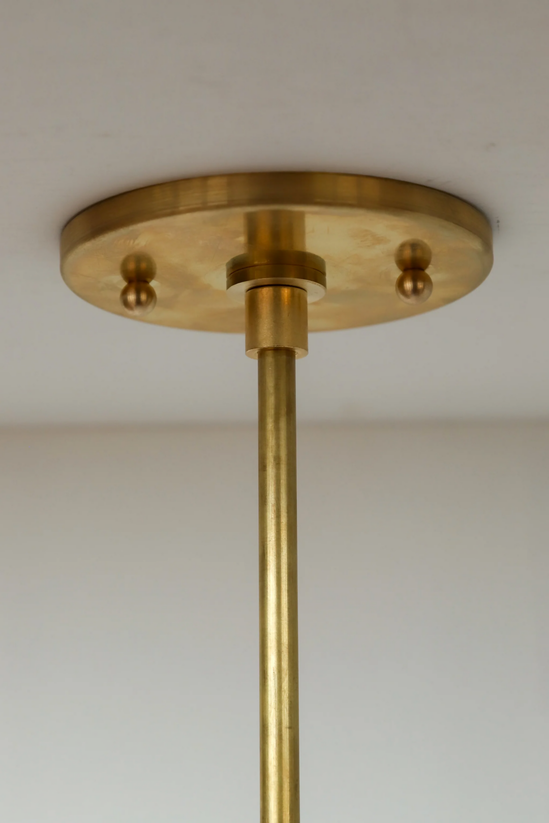 A close up of the golden hanging mount on a  white pleated pendant light hanging in a room with decorative walls, displaying a soft illumination, available  to buy on the-salon.com. SALON curates the finest , unique, handmade pieces from the interior industry's best makers and brands. Shop luxury furniture, lighting, rugs, art, antiques and vintage pieces and accessories from SALON interior designed rooms.
