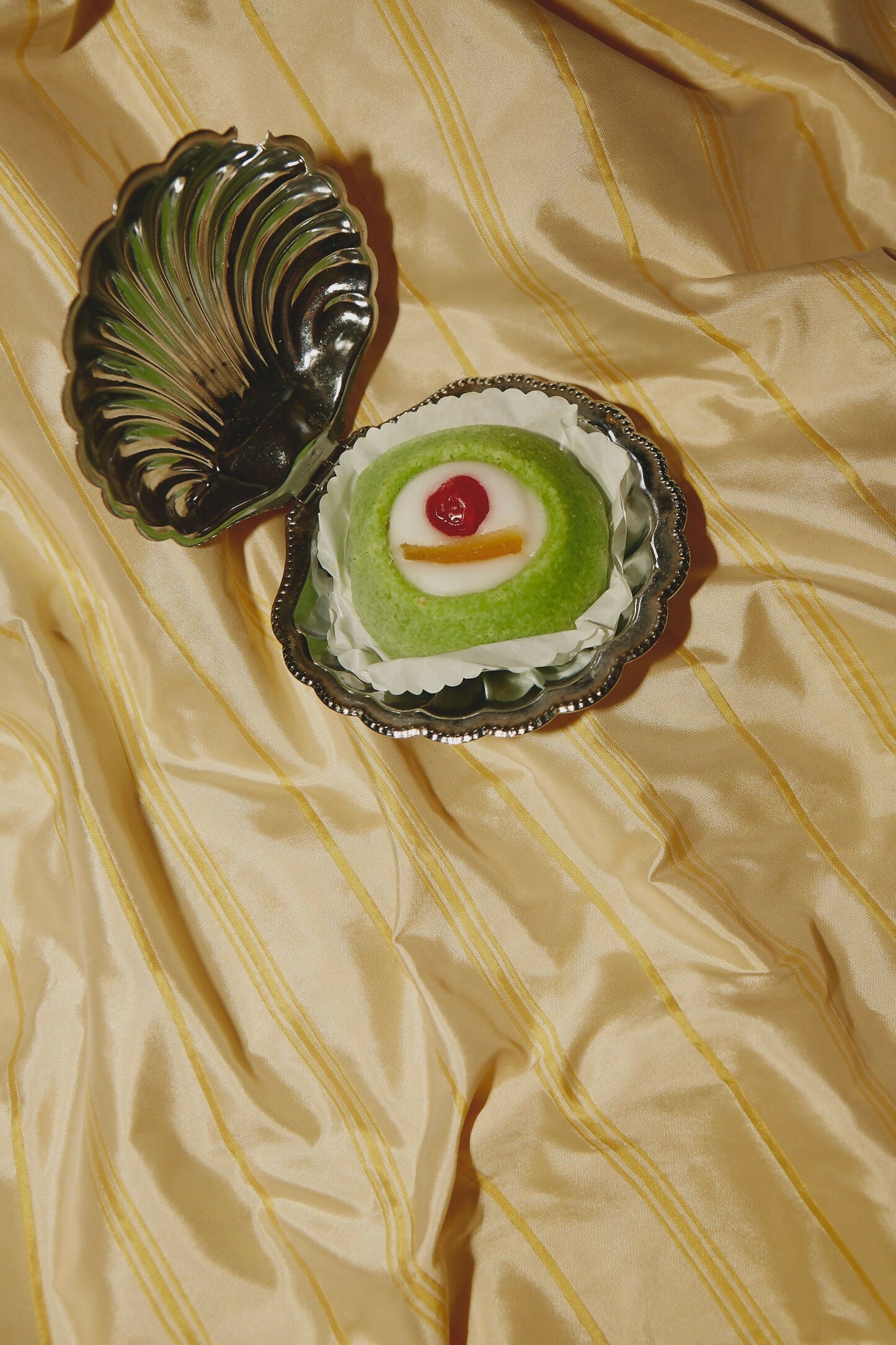 A close-up image of a yellow taffeta stripe fabric with a pin stripe pattern, underneath a silver clam-shaped box,  available  to buy on the-salon.com. SALON curates the finest , unique, handmade pieces from the interior industry's best makers and brands. Shop luxury furniture, lighting, rugs, art, antiques and vintage pieces and accessories from SALON interior designed rooms.