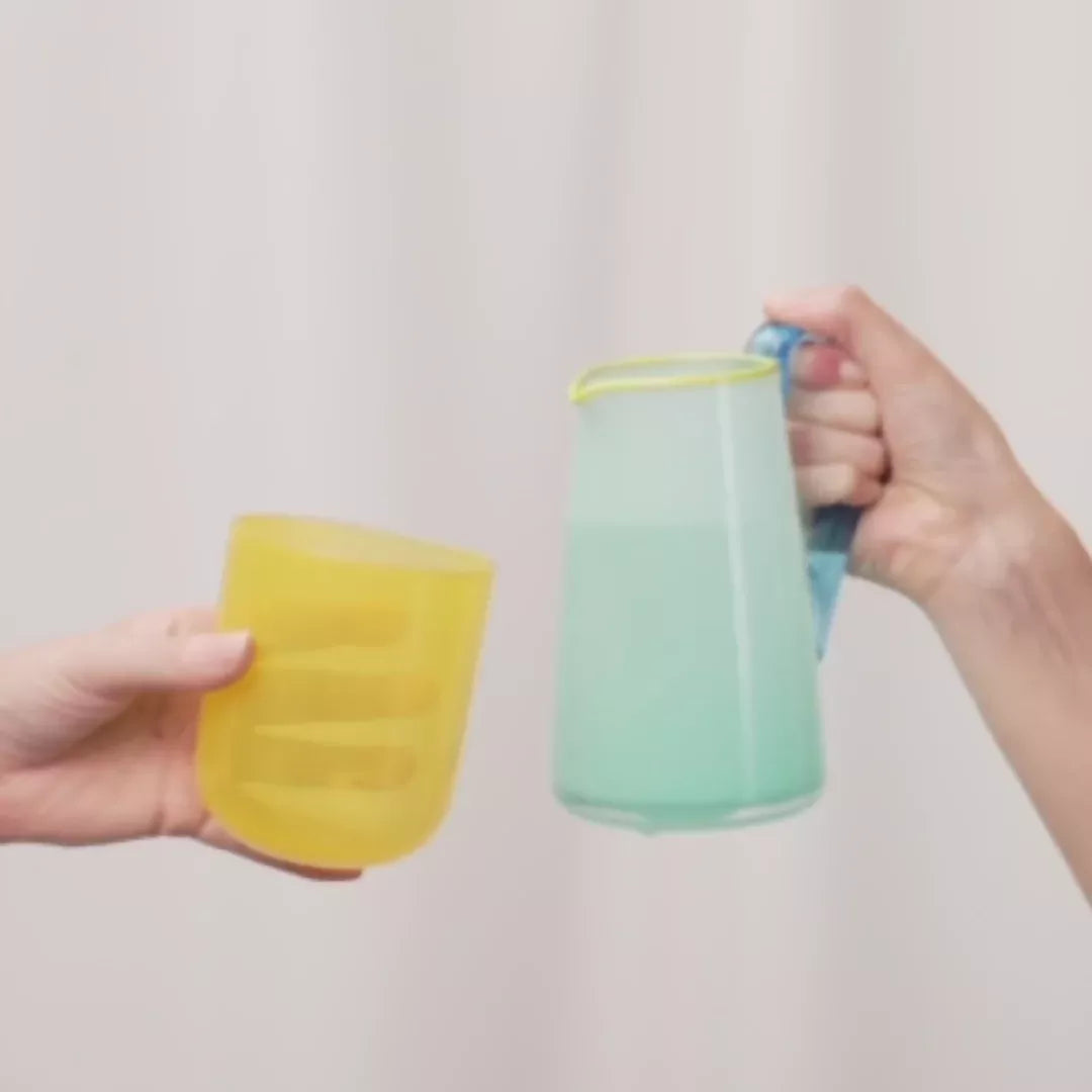 An image of the hand-blown blue glass milk jug with an aqua blue handle and a celadon lip, with the hand-blown yellow glass, available  to buy on the-salon.com. SALON curates the finest , unique, handmade pieces from the interior industry's best makers and brands. Shop luxury furniture, lighting, rugs, art, antiques and vintage pieces and accessories from SALON interior designed rooms.