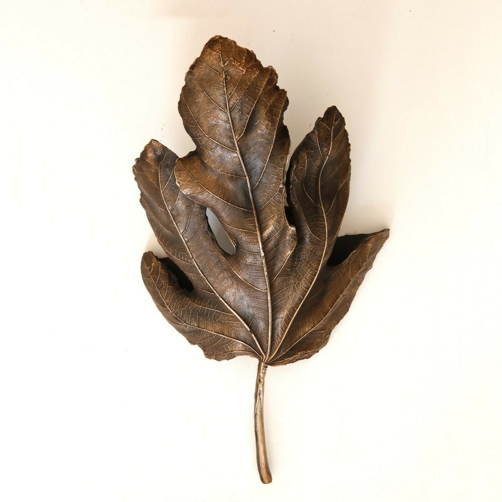 A brass wall light fixture designed to resemble a fig leaf, with a textured surface and a wall mounting bracket,  available  to buy on the-salon.com. SALON curates the finest , unique, handmade pieces from the interior industry's best makers and brands. Shop luxury furniture, lighting, rugs, art, antiques and vintage pieces and accessories from SALON interior designed rooms.