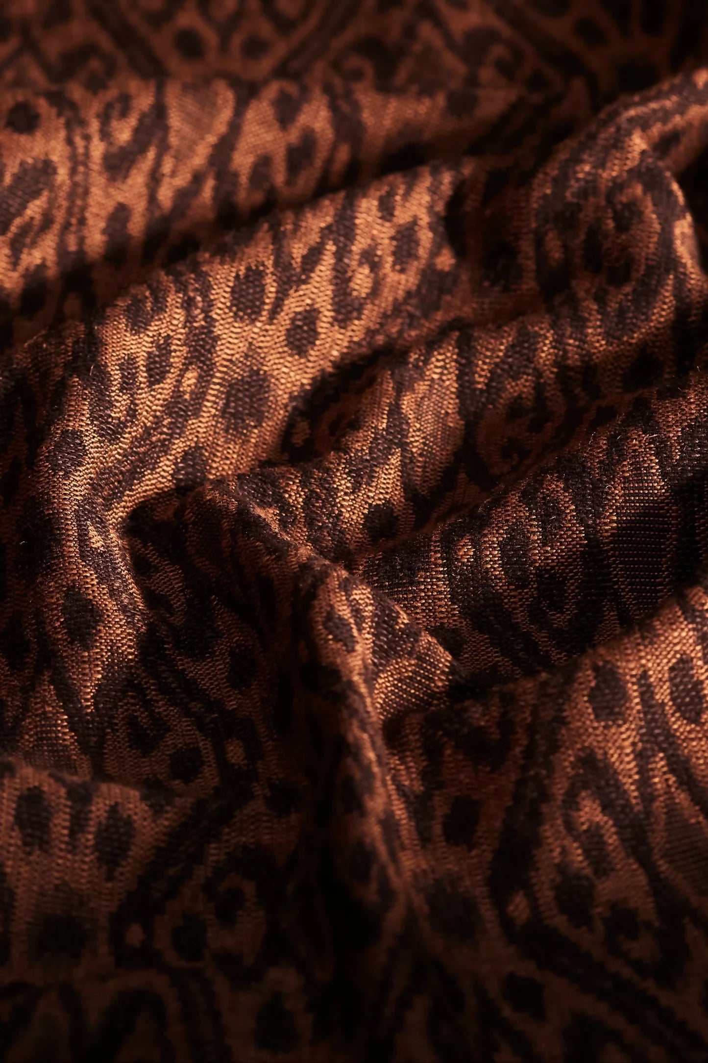 Close-up view of woven ikat fabric featuring a tortoiseshell pattern with shades of brown, gold, and orange,  available  to buy on the-salon.com. SALON curates the finest , unique, handmade pieces from the interior industry's best makers and brands. Shop luxury furniture, lighting, rugs, art, antiques and vintage pieces and accessories from SALON interior designed rooms.
