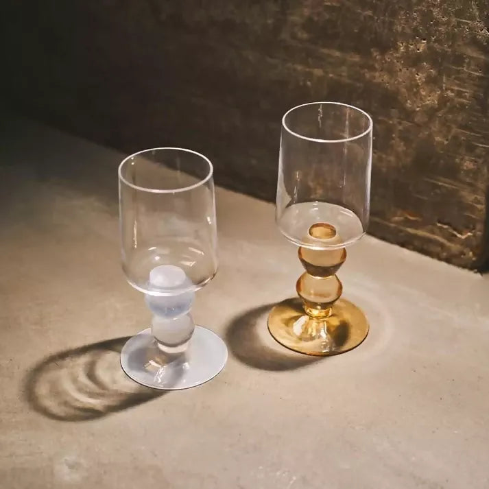 Two glasses with coloured bases on a textured surface, available  to buy on the-salon.com. SALON curates the finest , unique, handmade pieces from the interior industry's best makers and brands. Shop luxury furniture, lighting, rugs, art, antiques and vintage pieces and accessories from SALON interior designed rooms.