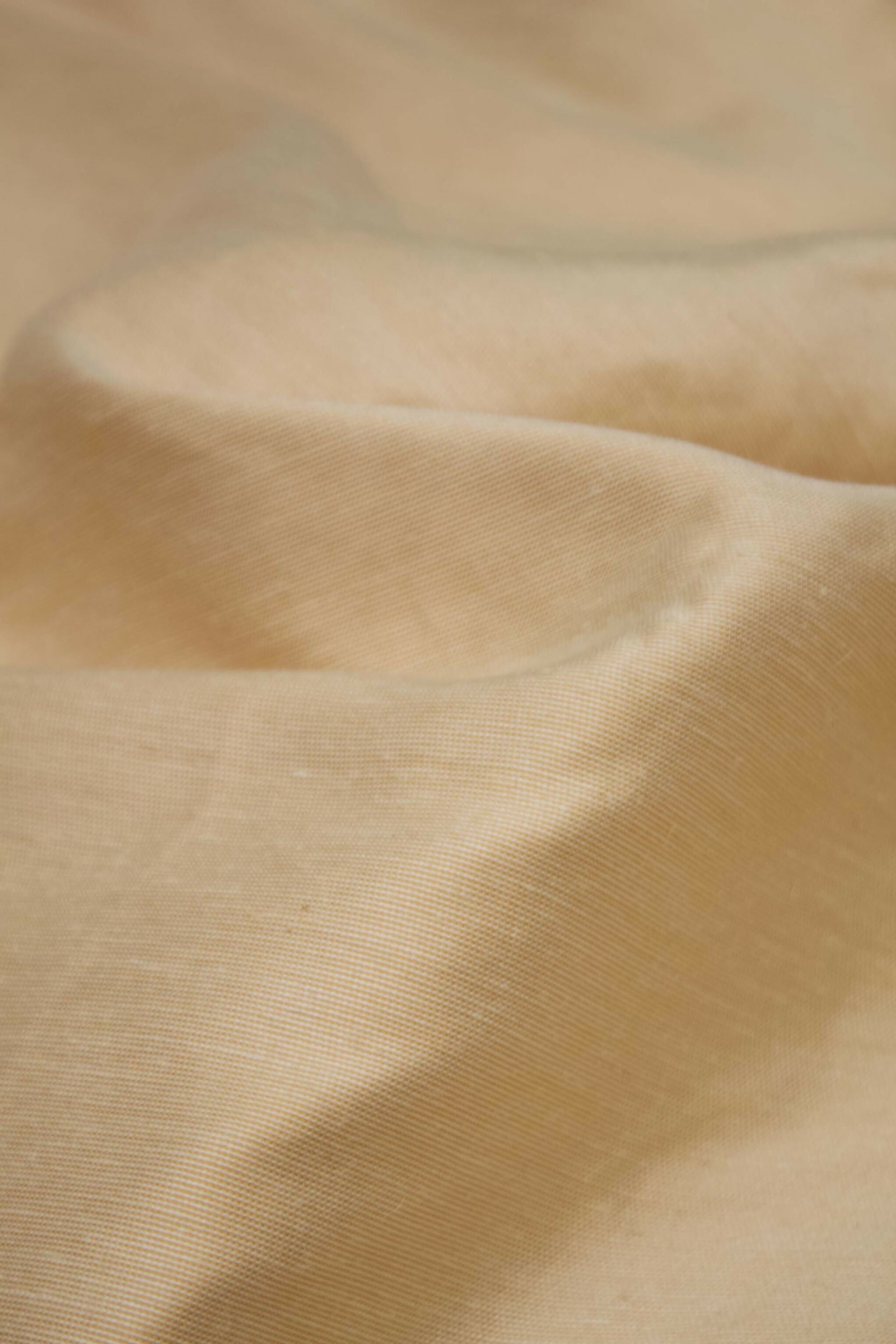Close-up of a silk sateen fabric in a pale honey colour, showing its texture and sheen,  available  to buy on the-salon.com. SALON curates the finest , unique, handmade pieces from the interior industry's best makers and brands. Shop luxury furniture, lighting, rugs, art, antiques and vintage pieces and accessories from SALON interior designed rooms.