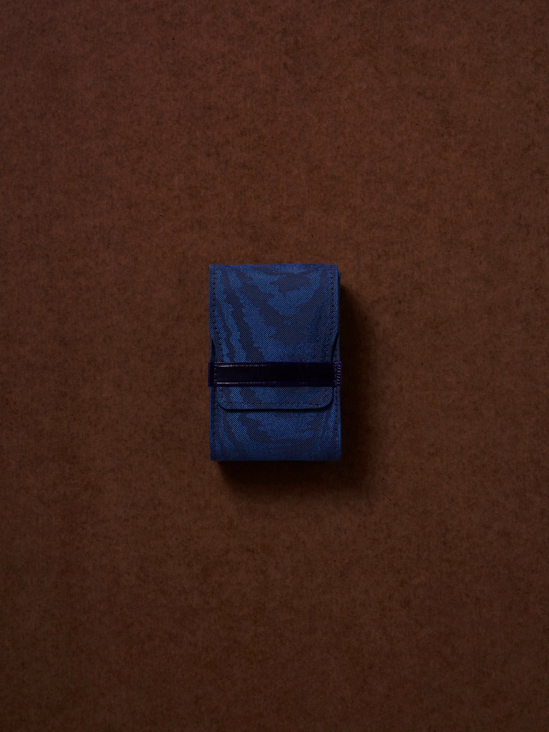 Blue fabric pouch with a black strap on a brown background,  available  to buy on the-salon.com. SALON curates the finest , unique, handmade pieces from the interior industry's best makers and brands. Shop luxury furniture, lighting, rugs, art, antiques and vintage pieces and accessories from SALON interior designed rooms.