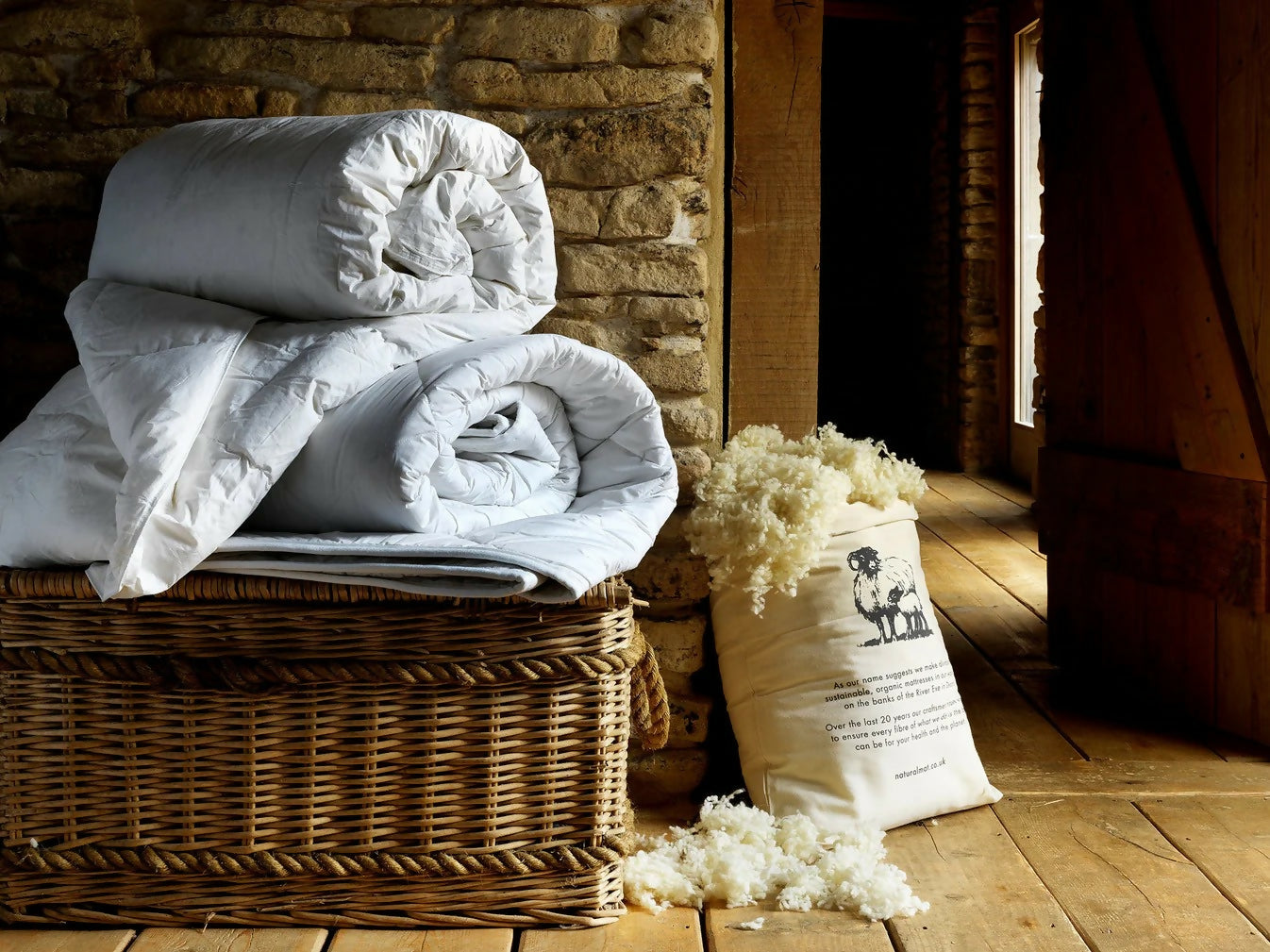 Stack of white blankets in a wicker basket against a stone wall, available to buy on the-salon.com. SALON curates the finest , unique, handmade pieces from the interior industry's best makers and brands. Shop luxury furniture, lighting, rugs, art, antiques and vintage pieces and accessories from SALON interior designed rooms.