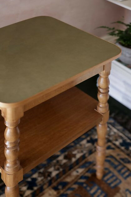 A brown wooden bedside table with a leather top, placed on a patterned carpet,  available  to buy on the-salon.com. SALON curates the finest , unique, handmade pieces from the interior industry's best makers and brands. Shop luxury furniture, lighting, rugs, art, antiques and vintage pieces and accessories from SALON interior designed rooms.