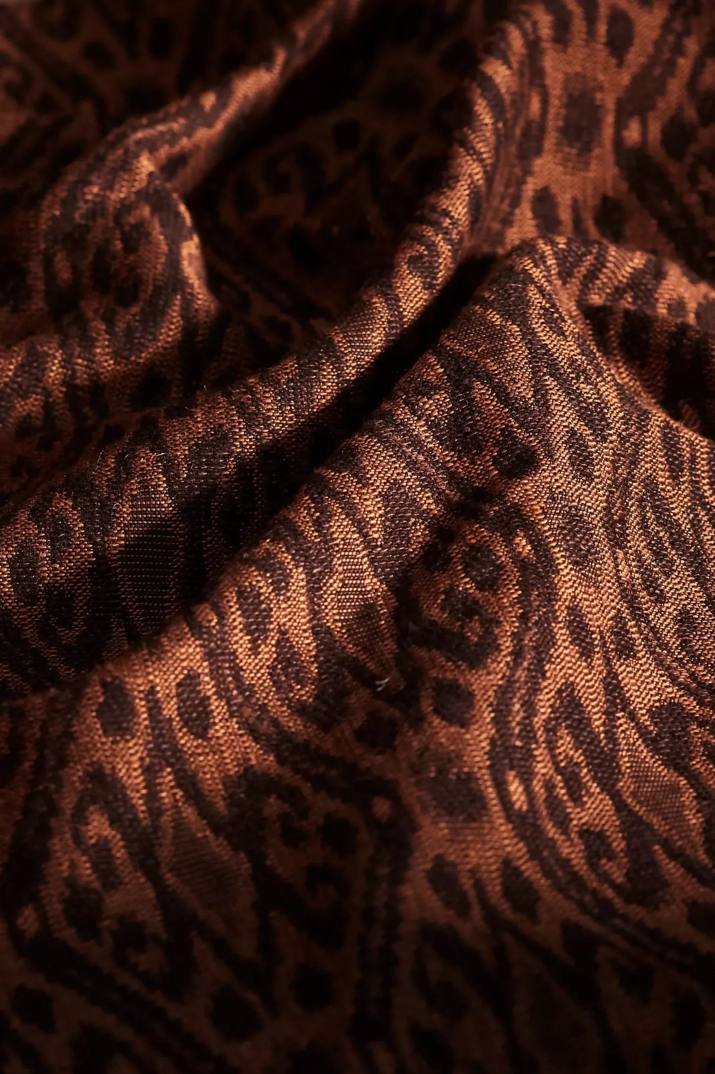 Close-up view of woven ikat fabric featuring a tortoiseshell pattern with shades of brown, gold, and orange,  available  to buy on the-salon.com. SALON curates the finest , unique, handmade pieces from the interior industry's best makers and brands. Shop luxury furniture, lighting, rugs, art, antiques and vintage pieces and accessories from SALON interior designed rooms.