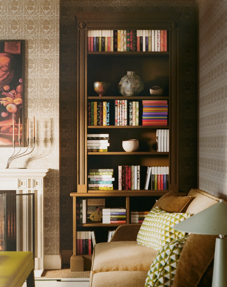 A wooden bookcase with reeded flanking columns and lion masks, featuring a stepped cornice, open shelves with books, and a lockable cupboard base, placed in a room with patterned wallpaper and a sofa,  available  to buy on the-salon.com. SALON curates the finest , unique, handmade pieces from the interior industry's best makers and brands. Shop luxury furniture, lighting, rugs, art, antiques and vintage pieces and accessories from SALON interior designed rooms.