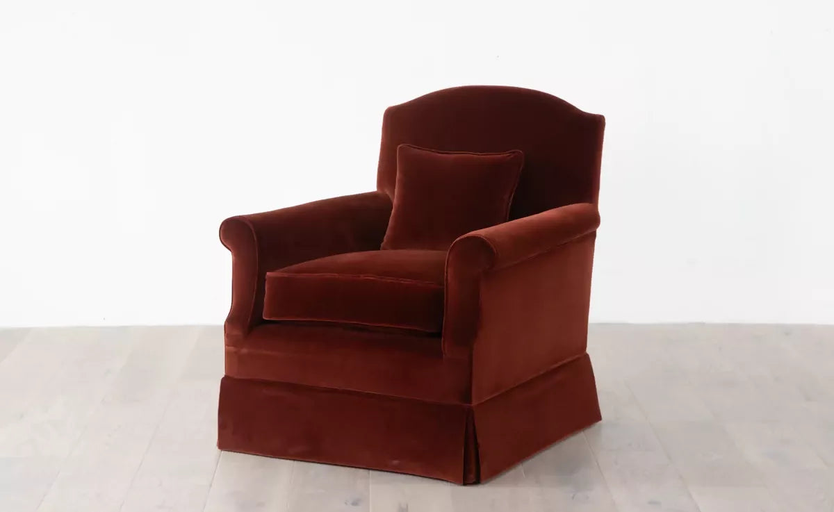 An elegant red upholstered armchair with a plush backrest and seat cushion, positioned angularly in front of a white background ,  available  to buy on the-salon.com. SALON curates the finest , unique, handmade pieces from the interior industry's best makers and brands. Shop luxury furniture, lighting, rugs, art, antiques and vintage pieces and accessories from SALON interior designed rooms.