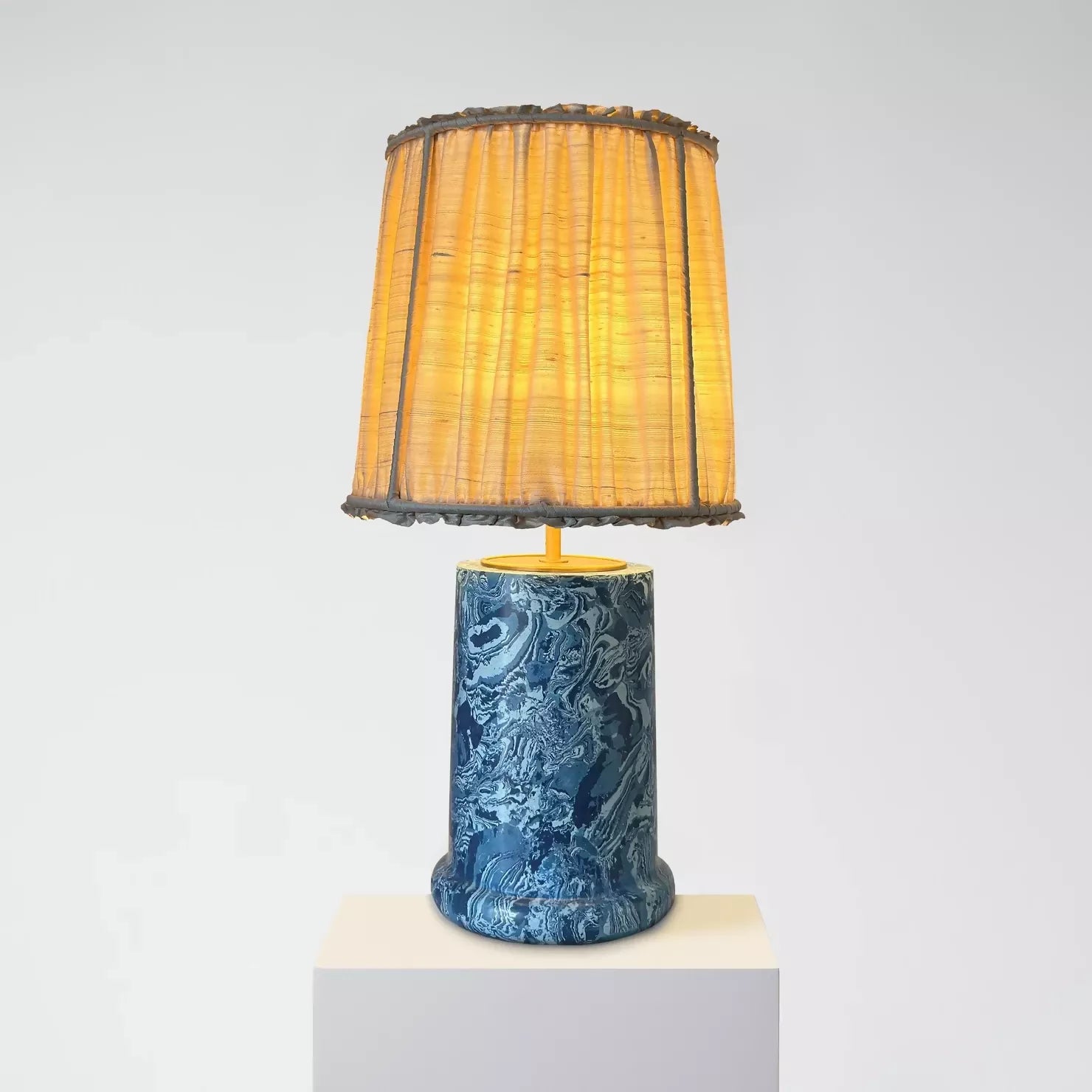 A blue marbled base table lamp with brass detailing, topped with a gold pleated shade,  available  to buy on the-salon.com. SALON curates the finest , unique, handmade pieces from the interior industry's best makers and brands. Shop luxury furniture, lighting, rugs, art, antiques and vintage pieces and accessories from SALON interior designed rooms.