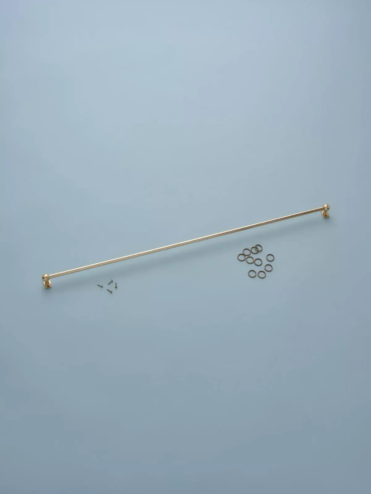 Gold curtain rod with hardware on a light blue background,  available  to buy on the-salon.com. SALON curates the finest , unique, handmade pieces from the interior industry's best makers and brands. Shop luxury furniture, lighting, rugs, art, antiques and vintage pieces and accessories from SALON interior designed rooms.