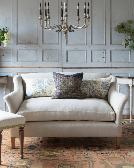 Beige sofa with decorative pillows in a room with floral arrangements and a chandelier.