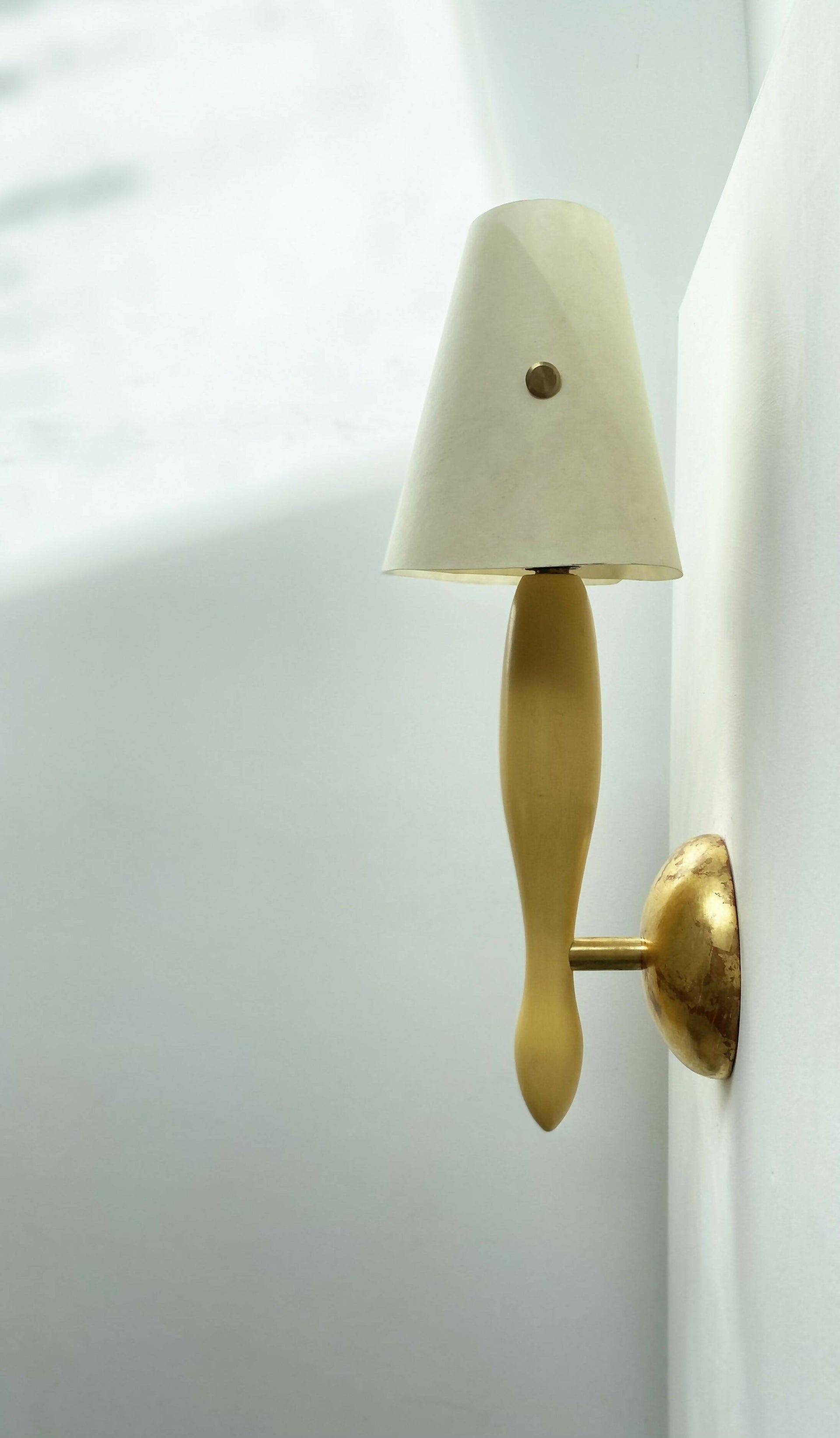 A wall light fixture with a Yellow, stem-like structure and a white conical shade, mounted on a gold-colored plate, available  to buy on the-salon.com. SALON curates the finest , unique, handmade pieces from the interior industry's best makers and brands. Shop luxury furniture, lighting, rugs, art, antiques and vintage pieces and accessories from SALON interior designed rooms.