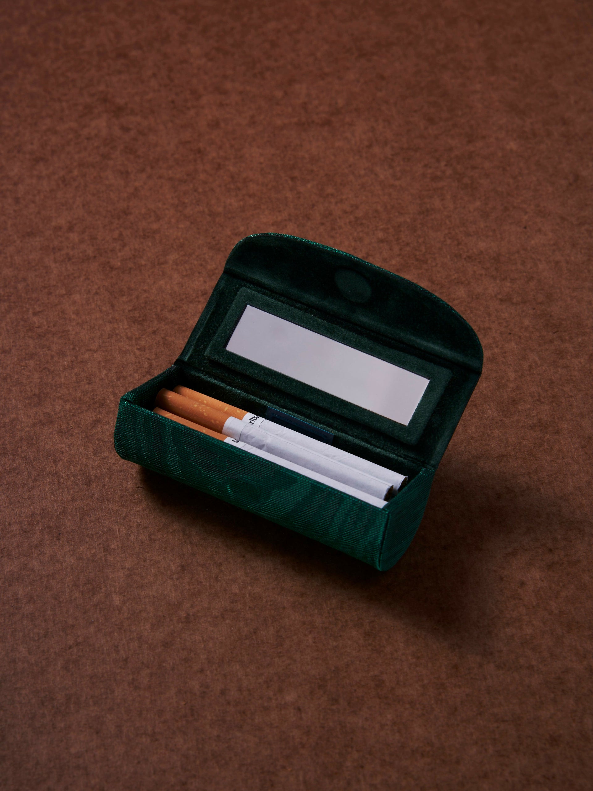 Open green velvet cigarette case with cigarettes on a brown background,  available  to buy on the-salon.com. SALON curates the finest , unique, handmade pieces from the interior industry's best makers and brands. Shop luxury furniture, lighting, rugs, art, antiques and vintage pieces and accessories from SALON interior designed rooms.