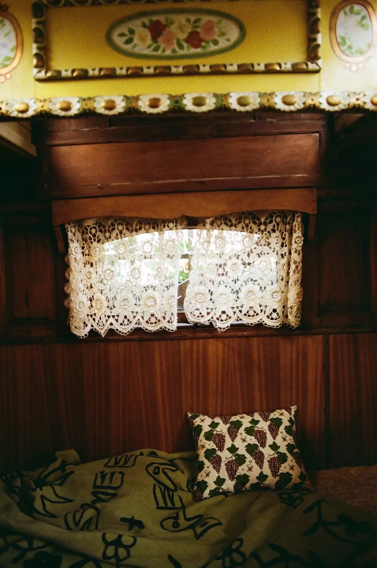 A rectangular cushion with a floral pattern featuring purple grapes and green leaves, placed on a green textile,  available  to buy on the-salon.com. SALON curates the finest , unique, handmade pieces from the interior industry's best makers and brands. Shop luxury furniture, lighting, rugs, art, antiques and vintage pieces and accessories from SALON interior designed rooms.