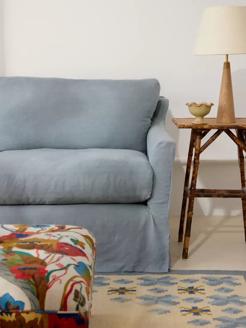 Light blue sofa in a living room with a floral-patterned ottoman and a wooden side table.