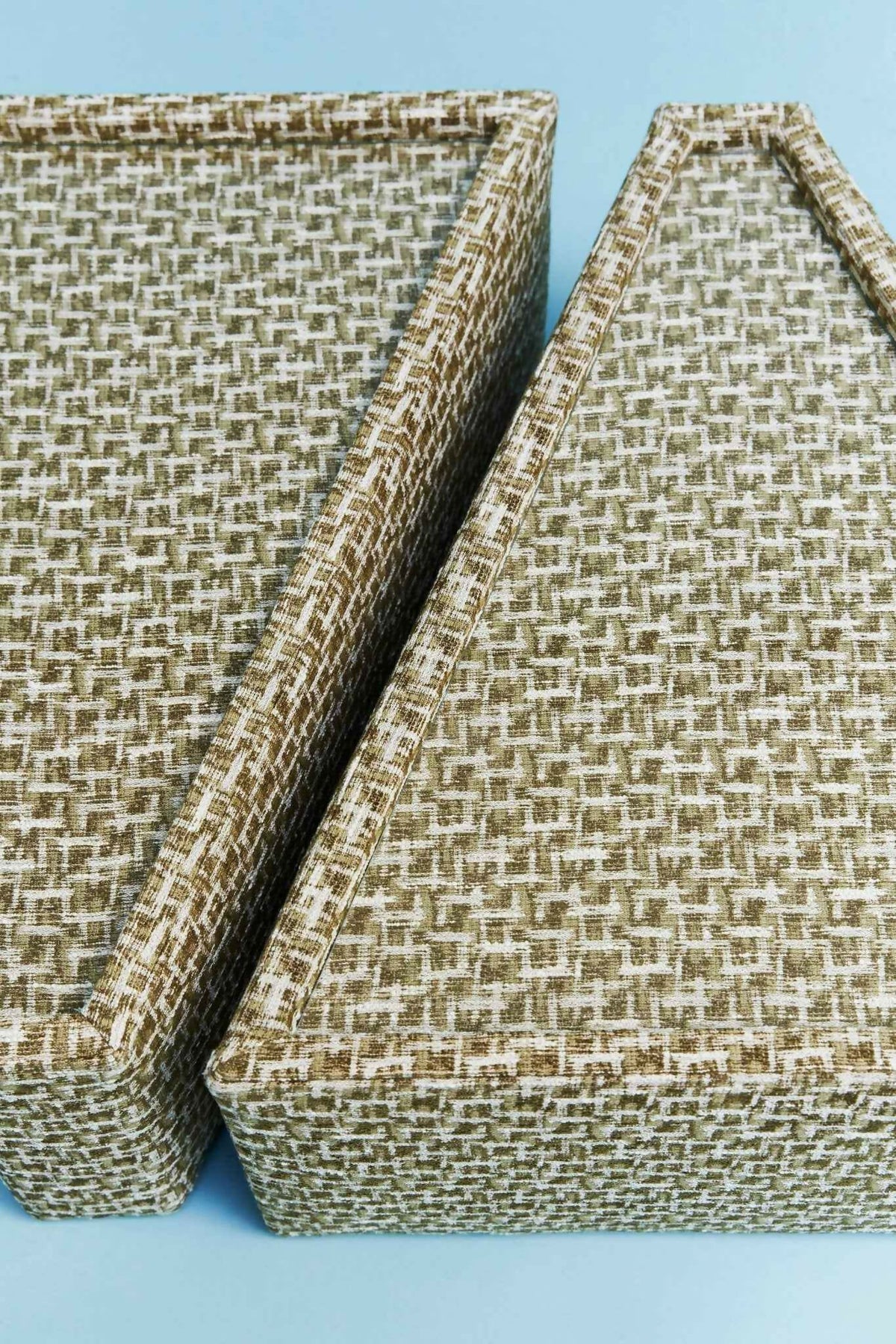 Two woven storage baskets with a textured basketweave pattern in beige and brown, shown on a light blue background.