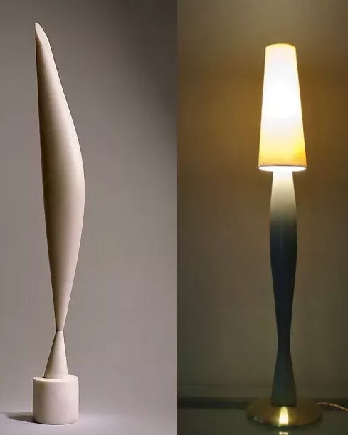 A sculptural table lamp shown in two views: a tall, narrow cream-colored shade on a cylindrical base against a neutral gray background, and a second view showing the lamp lit with a glowing tapered shade and a blue-gray twisted stem on a gold-toned base.