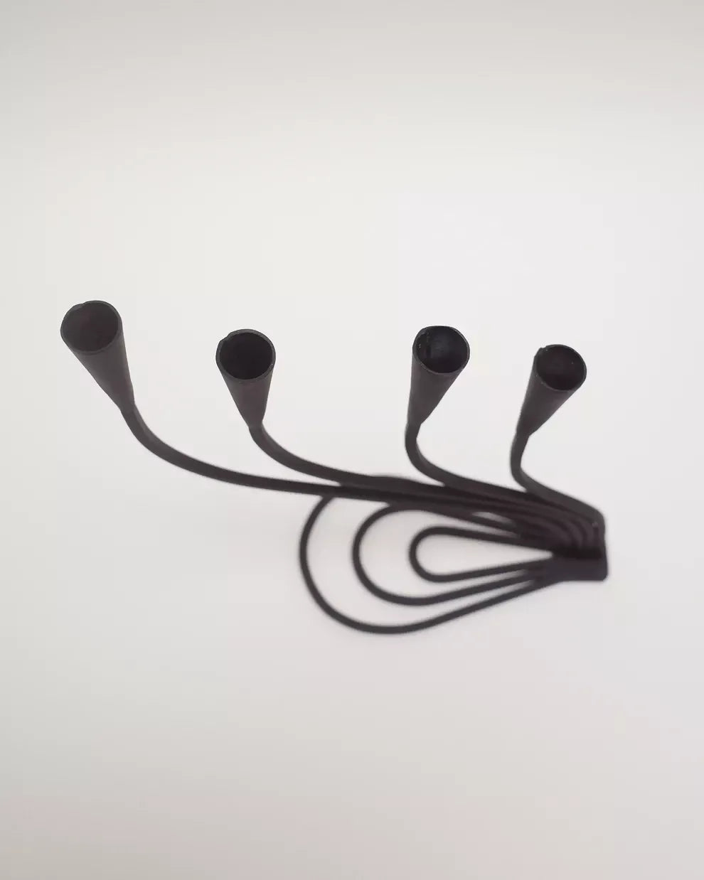 A black, hand forged iron candle holder with four curved arms and cone shaped heads, on a white background,  available  to buy on the-salon.com. SALON curates the finest , unique, handmade pieces from the interior industry's best makers and brands. Shop luxury furniture, lighting, rugs, art, antiques and vintage pieces and accessories from SALON interior designed rooms.