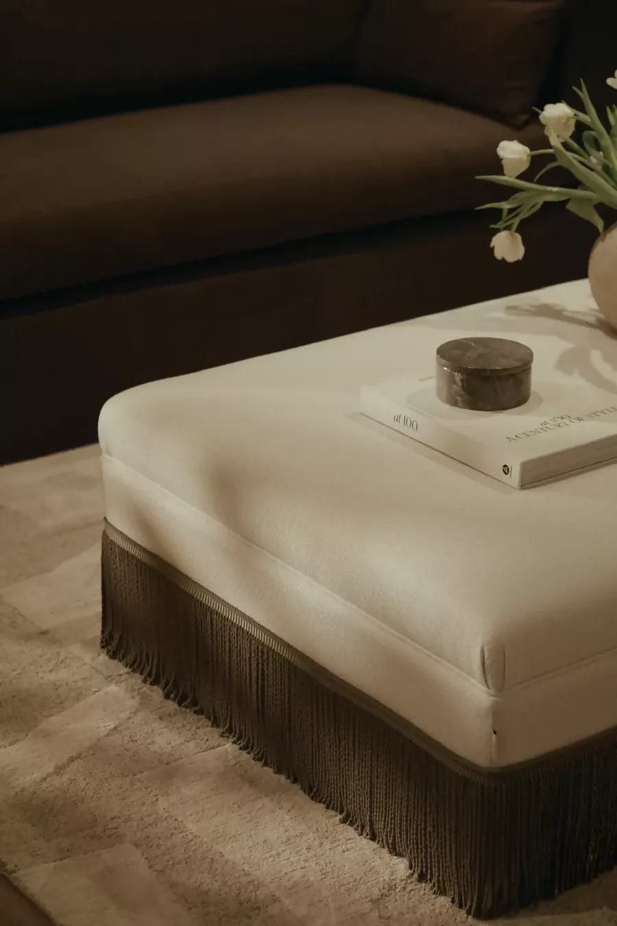 Beige ottoman with fringe details in a living room setting