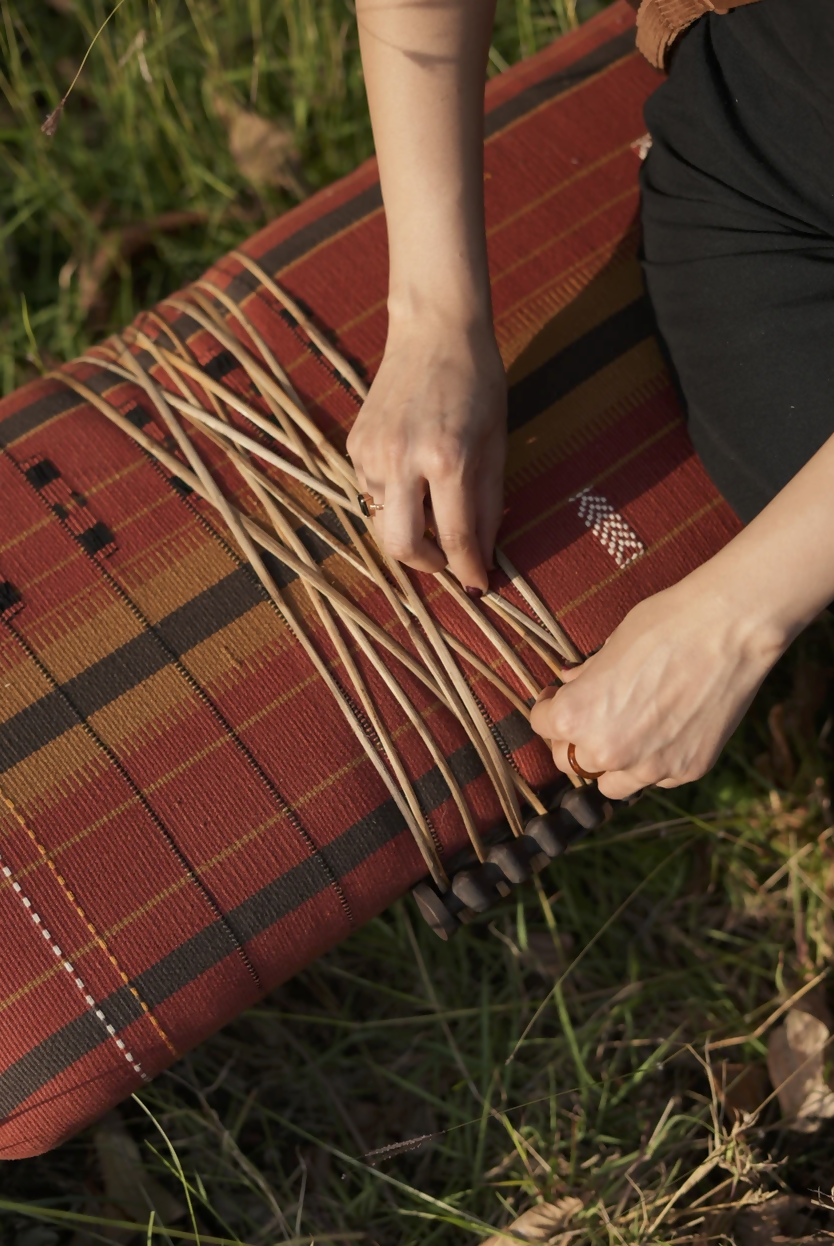 Person working on a woven mat with grass in the background,  available  to buy on the-salon.com. SALON curates the finest , unique, handmade pieces from the interior industry's best makers and brands. Shop luxury furniture, lighting, rugs, art, antiques and vintage pieces and accessories from SALON interior designed rooms.