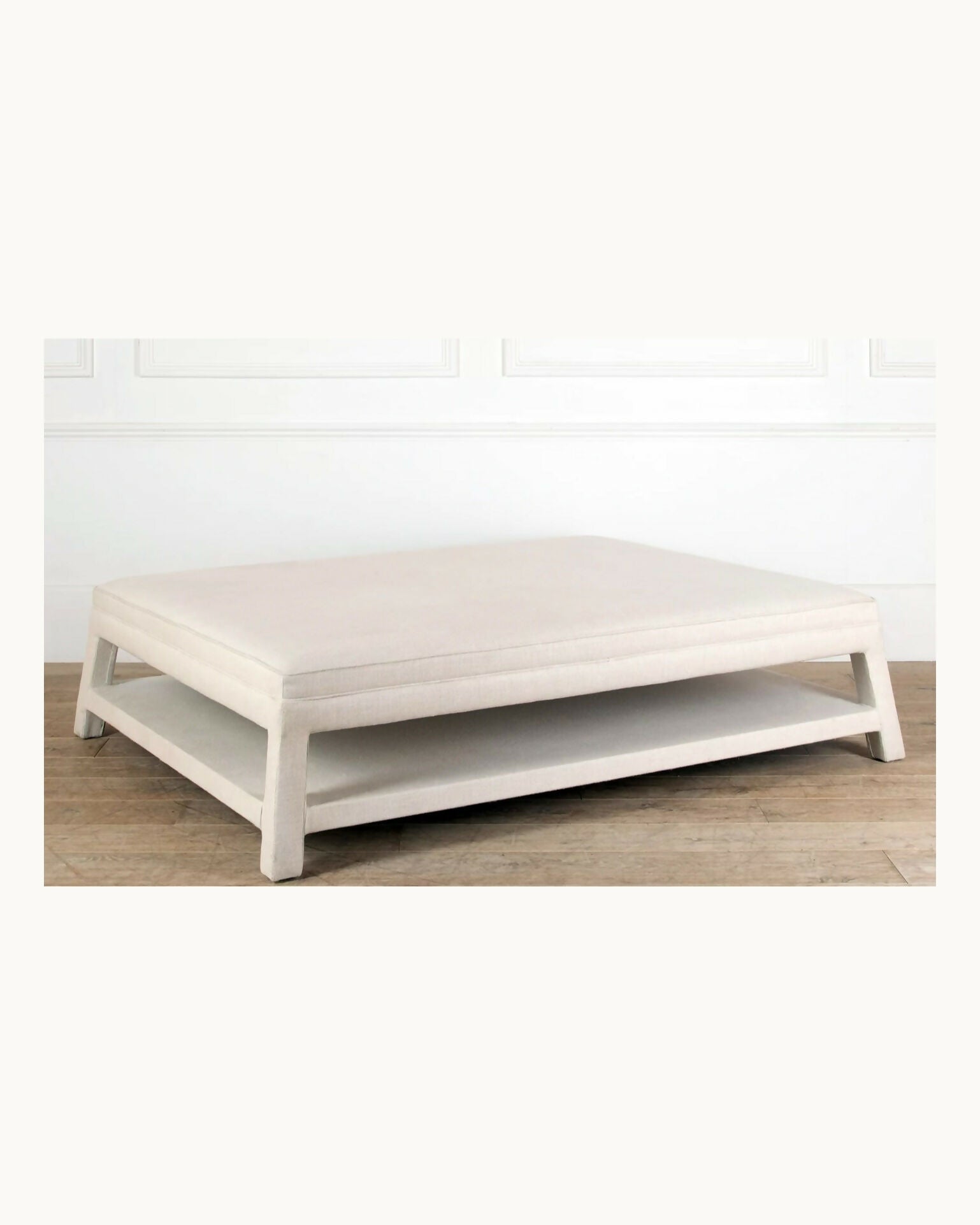 White ottoman on a wooden floor with a white wall background,  available  to buy on the-salon.com. SALON curates the finest , unique, handmade pieces from the interior industry's best makers and brands. Shop luxury furniture, lighting, rugs, art, antiques and vintage pieces and accessories from SALON interior designed rooms.