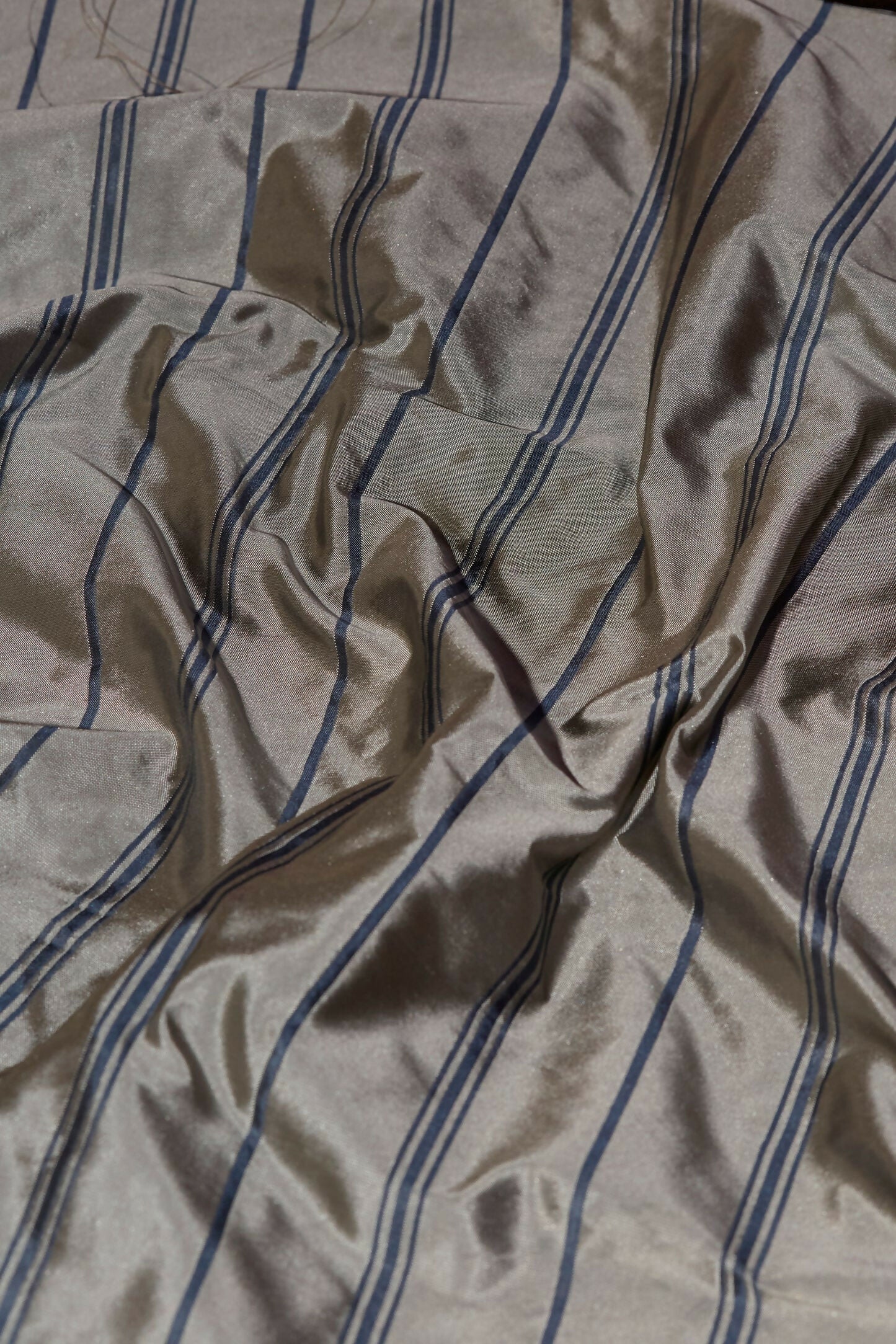 Close-up view of tafta stripe fabric in grey showcasing its navy blue stripes, texture and reflective quality,  available  to buy on the-salon.com. SALON curates the finest , unique, handmade pieces from the interior industry's best makers and brands. Shop luxury furniture, lighting, rugs, art, antiques and vintage pieces and accessories from SALON interior designed rooms.