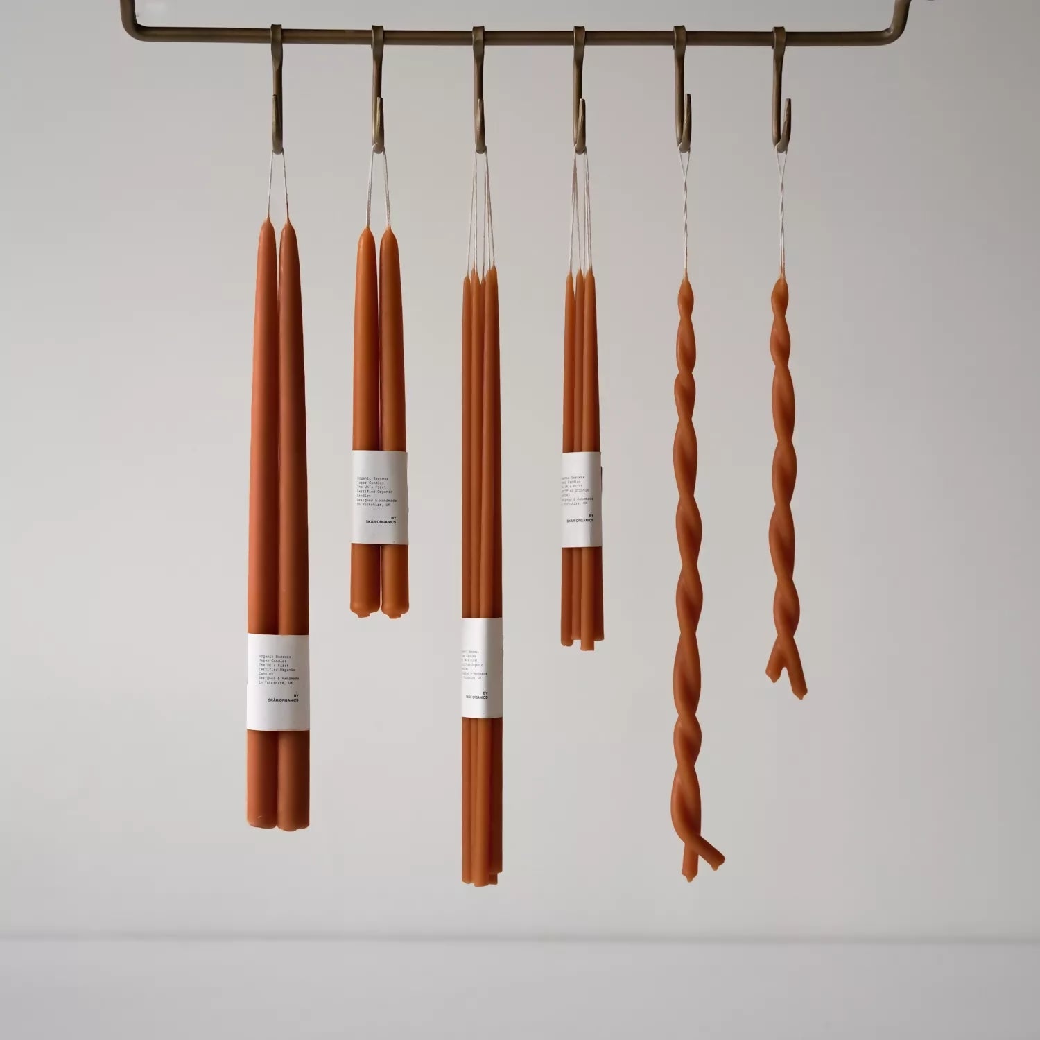 A selection of hand-dipped beeswax dinner candles in paprika color, hanging on a rack, with packaging around the base,  available  to buy on the-salon.com. SALON curates the finest , unique, handmade pieces from the interior industry's best makers and brands. Shop luxury furniture, lighting, rugs, art, antiques and vintage pieces and accessories from SALON interior designed rooms.