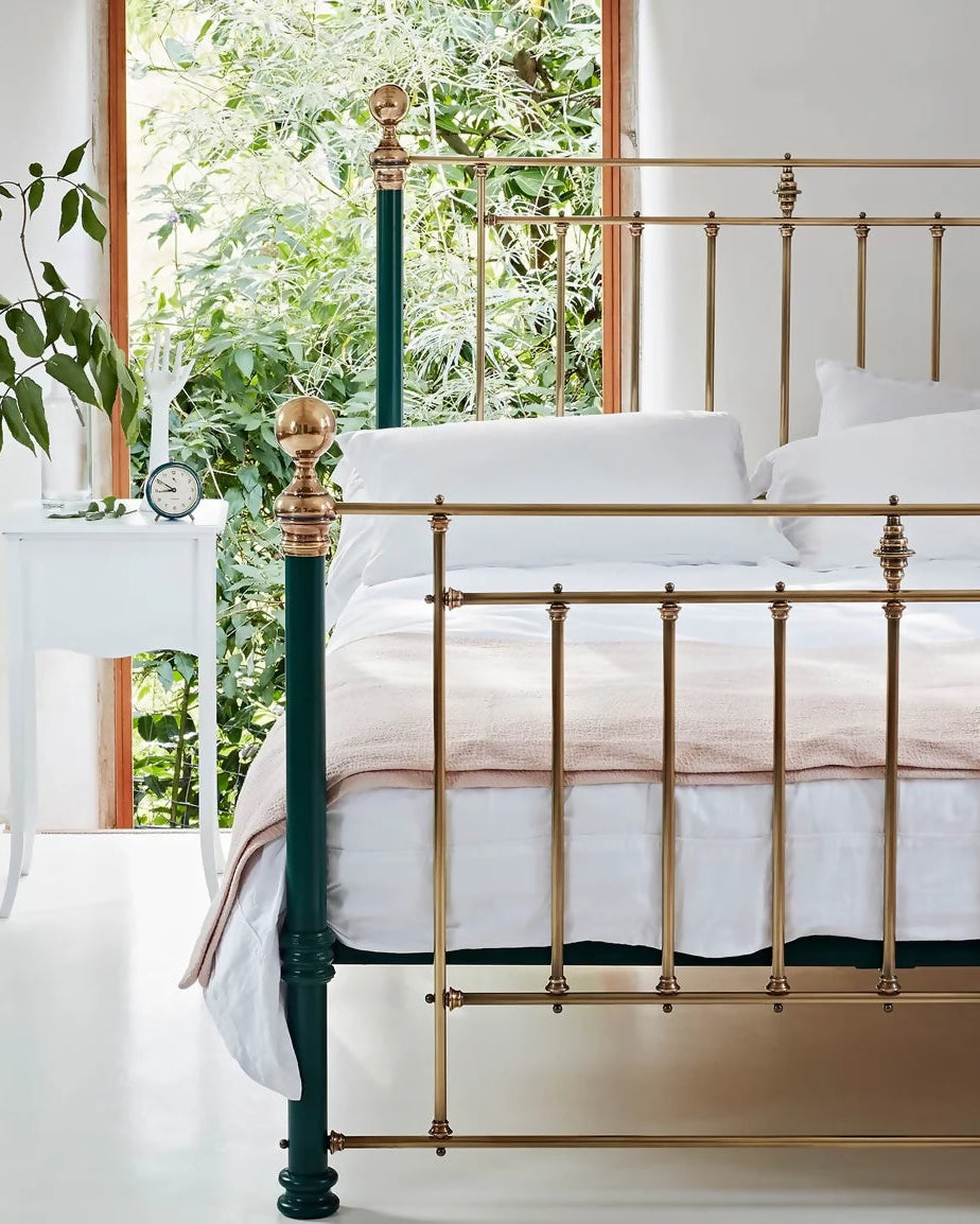 Gold and green metal bed frame with white bedding and a floral blanket in a bright bedroom.