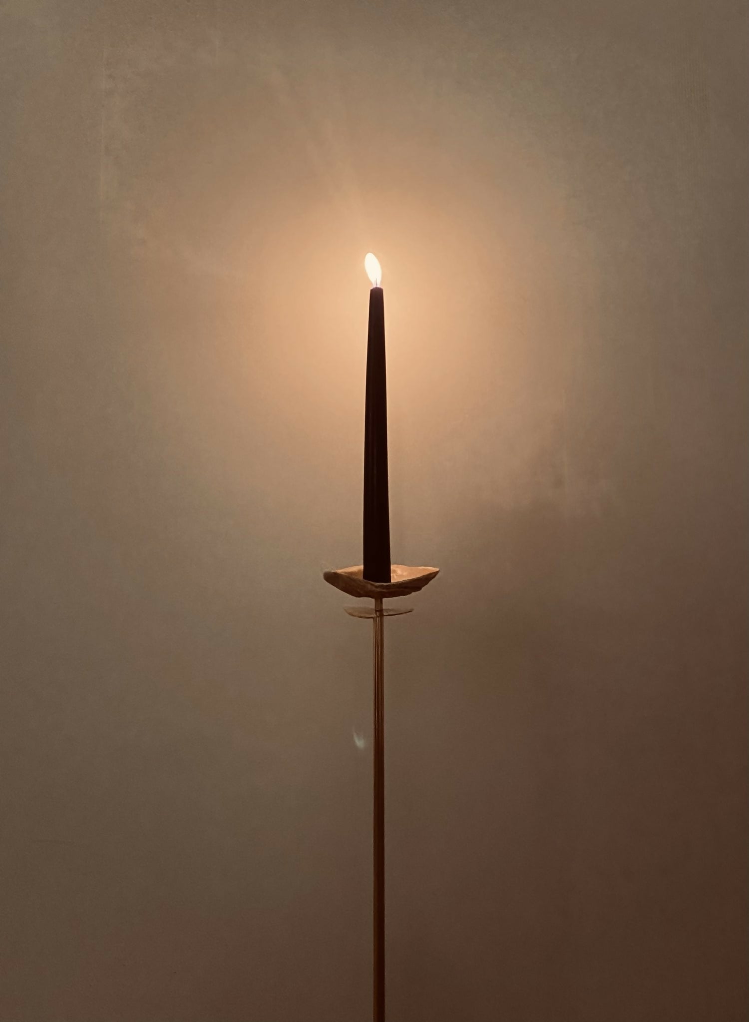 A brass candlestick with a shell design, featuring a lit candle, raised from a milled brass dome base, with a hand-cut brass sheet planished to create contours reflecting light, available  to buy on the-salon.com. SALON curates the finest , unique, handmade pieces from the interior industry's best makers and brands. Shop luxury furniture, lighting, rugs, art, antiques and vintage pieces and accessories from SALON interior designed rooms.