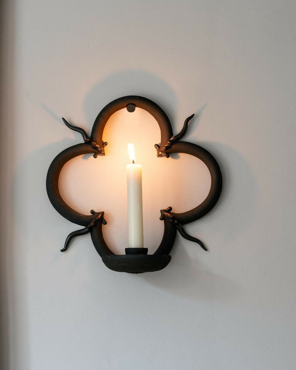 Decorative wall sconce with a candle on a white wall next to patterned wallpaper,  available  to buy on the-salon.com. SALON curates the finest , unique, handmade pieces from the interior industry's best makers and brands. Shop luxury furniture, lighting, rugs, art, antiques and vintage pieces and accessories from SALON interior designed rooms.
