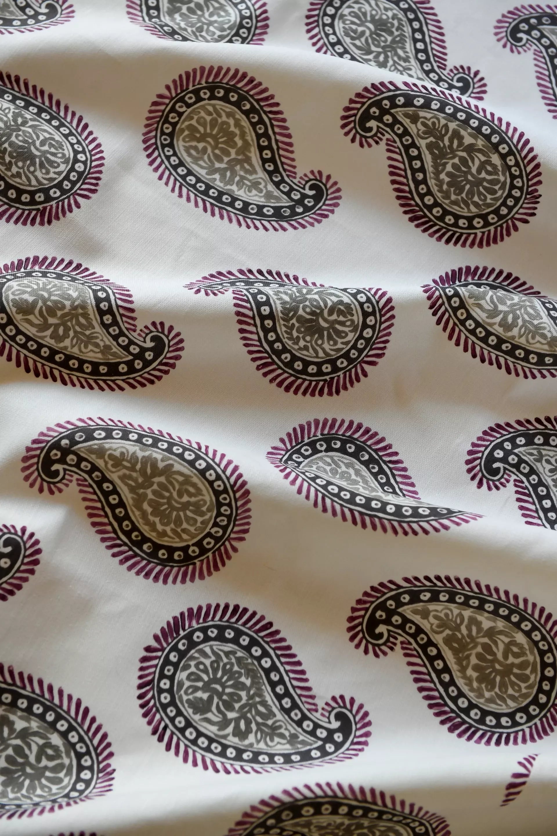 Close-up of a paisley patterned fabric with a design consisting of teardrop shapes and floral elements, predominantly in dark colors on a light background,available  to buy on the-salon.com. SALON curates the finest , unique, handmade pieces from the interior industry's best makers and brands. Shop luxury furniture, lighting, rugs, art, antiques and vintage pieces and accessories from SALON interior designed rooms