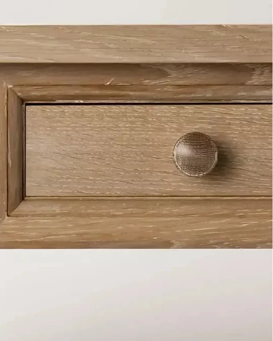 Close-up on the drawer on a  rectangular wooden refectory table with a drawer at each end and columnar supports, designed in a natural brown finish,  available  to buy on the-salon.com. SALON curates the finest , unique, handmade pieces from the interior industry's best makers and brands. Shop luxury furniture, lighting, rugs, art, antiques and vintage pieces and accessories from SALON interior designed rooms.