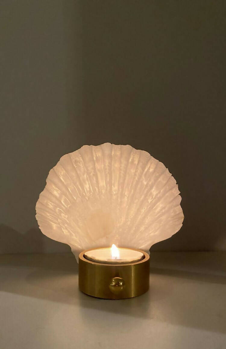 A white scallop shell tea light holder with a gold accent on the bottom, reflecting a soft light,  available  to buy on the-salon.com. SALON curates the finest , unique, handmade pieces from the interior industry's best makers and brands. Shop luxury furniture, lighting, rugs, art, antiques and vintage pieces and accessories from SALON interior designed rooms.