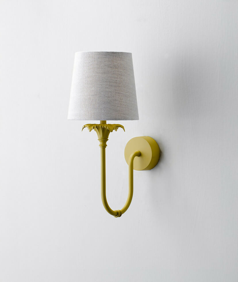A wall-mounted light fixture with a yellow-colored metal arm and a white, solid-patterned lampshade,  available  to buy on the-salon.com. SALON curates the finest , unique, handmade pieces from the interior industry's best makers and brands. Shop luxury furniture, lighting, rugs, art, antiques and vintage pieces and accessories from SALON interior designed rooms.