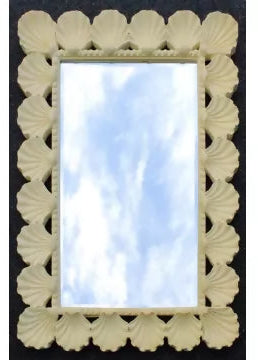 A rectangular decorative mirror with a cream-colored frame made of repeating scallop or shell-like motifs, reflecting a blue sky with clouds.