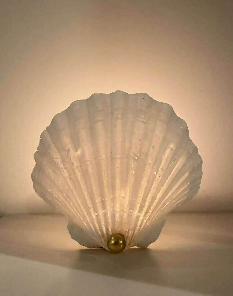 A white scallop shell tea light holder with a gold accent on the bottom, reflecting a soft light,  available  to buy on the-salon.com. SALON curates the finest , unique, handmade pieces from the interior industry's best makers and brands. Shop luxury furniture, lighting, rugs, art, antiques and vintage pieces and accessories from SALON interior designed rooms.