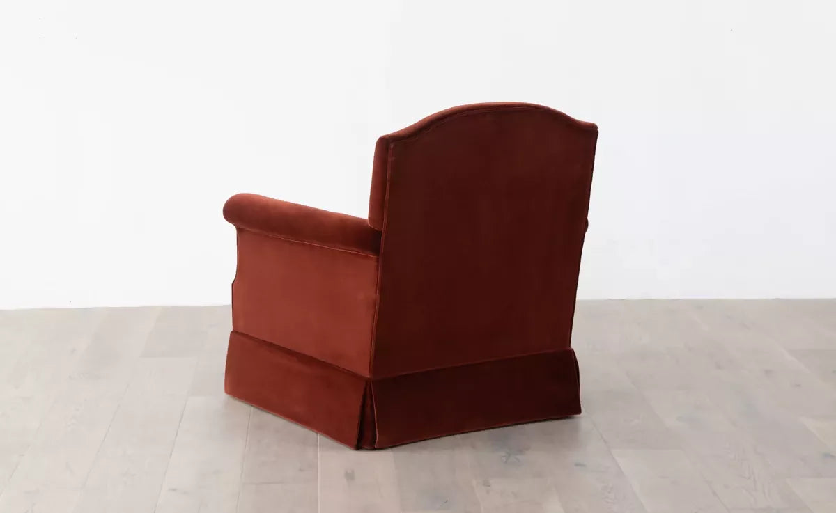 An elegant red upholstered armchair with a plush backrest and seat cushion, positioned  angularly in front of a white background,  available  to buy on the-salon.com. SALON curates the finest , unique, handmade pieces from the interior industry's best makers and brands. Shop luxury furniture, lighting, rugs, art, antiques and vintage pieces and accessories from SALON interior designed rooms.
