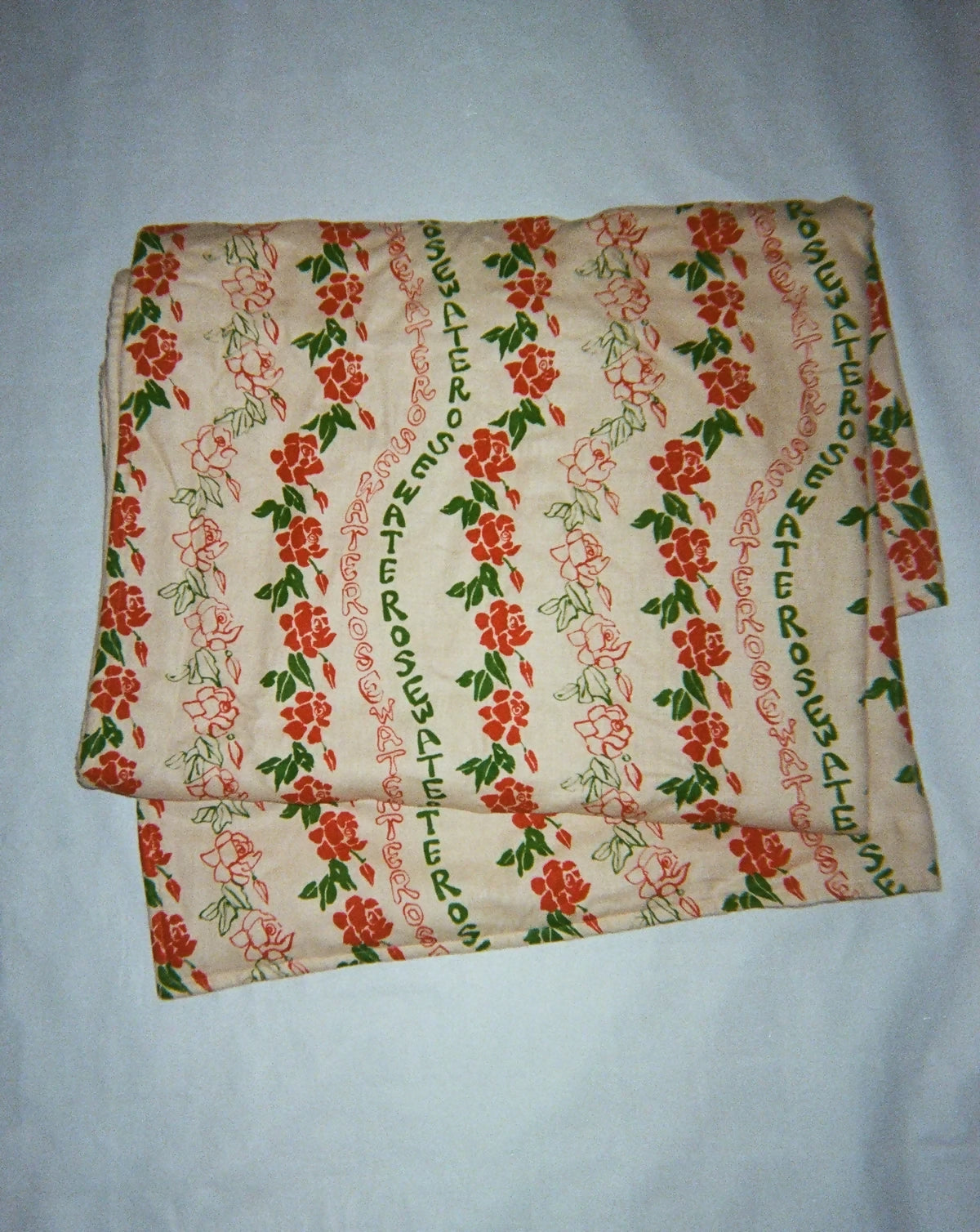 A folded quilt with a floral pattern featuring roses in red and green colors on a beige background,  available  to buy on the-salon.com. SALON curates the finest , unique, handmade pieces from the interior industry's best makers and brands. Shop luxury furniture, lighting, rugs, art, antiques and vintage pieces and accessories from SALON interior designed rooms.