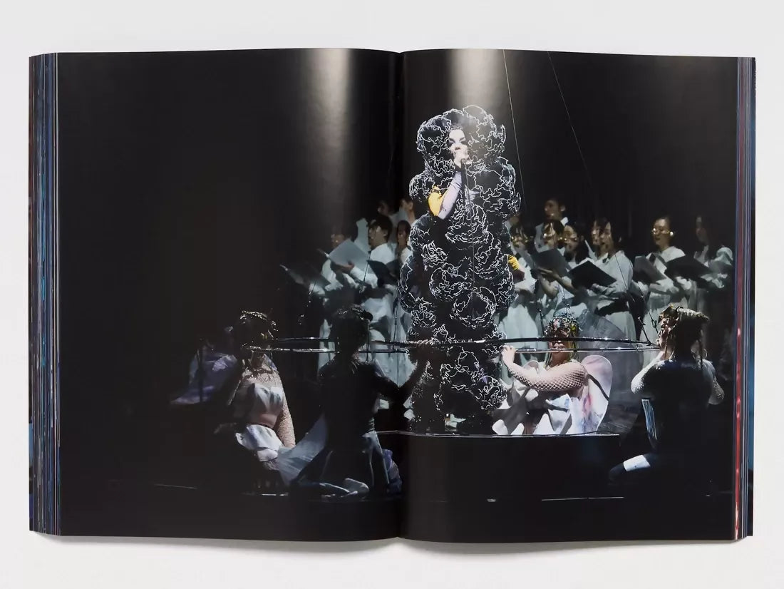 An image of an open book with an image of a woman singing on stage in a black frilly outfit, barely able to see her with the spotlight on her and a choir in the background, available  to buy on the-salon.com. SALON curates the finest , unique, handmade pieces from the interior industry's best makers and brands. Shop luxury furniture, lighting, rugs, art, antiques and vintage pieces and accessories from SALON interior designed rooms.