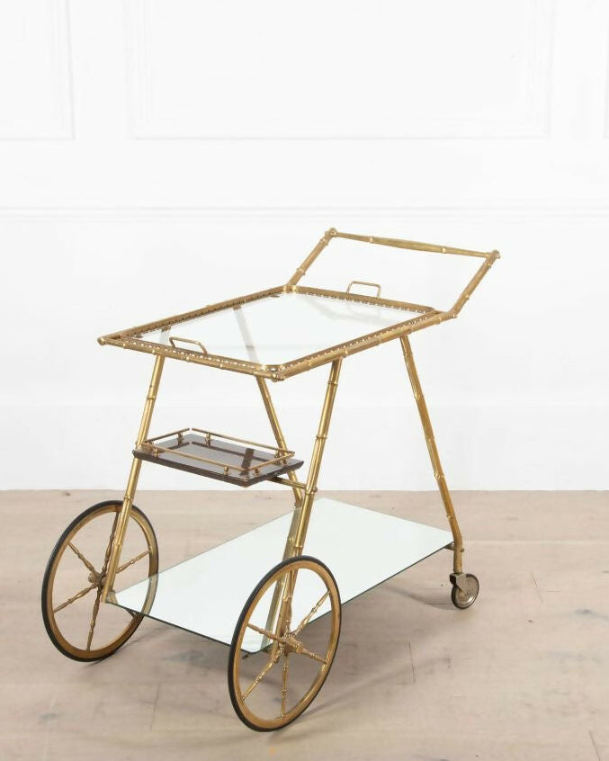 Gold bar cart with glass top on a light wooden floor.