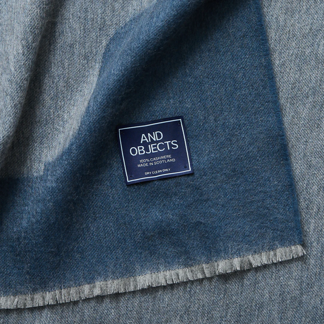 A folded slate blue cashmere throw blanket with a decorative border detail,  available  to buy on the-salon.com. SALON curates the finest , unique, handmade pieces from the interior industry's best makers and brands. Shop luxury furniture, lighting, rugs, art, antiques and vintage pieces and accessories from SALON interior designed rooms.