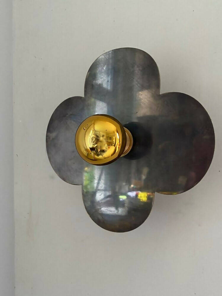 A wall light fixture with a gold-colored top and black, quatrefoil-shaped base,  available  to buy on the-salon.com. SALON curates the finest , unique, handmade pieces from the interior industry's best makers and brands. Shop luxury furniture, lighting, rugs, art, antiques and vintage pieces and accessories from SALON interior designed rooms.