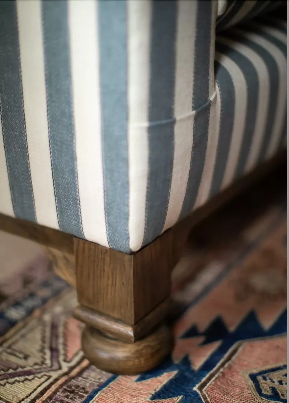A blue and white striped camel back sofa with solid oak turned legs in a room with decorative items on top, available  to buy on the-salon.com. SALON curates the finest , unique, handmade pieces from the interior industry's best makers and brands. Shop luxury furniture, lighting, rugs, art, antiques and vintage pieces and accessories from SALON interior designed rooms.
