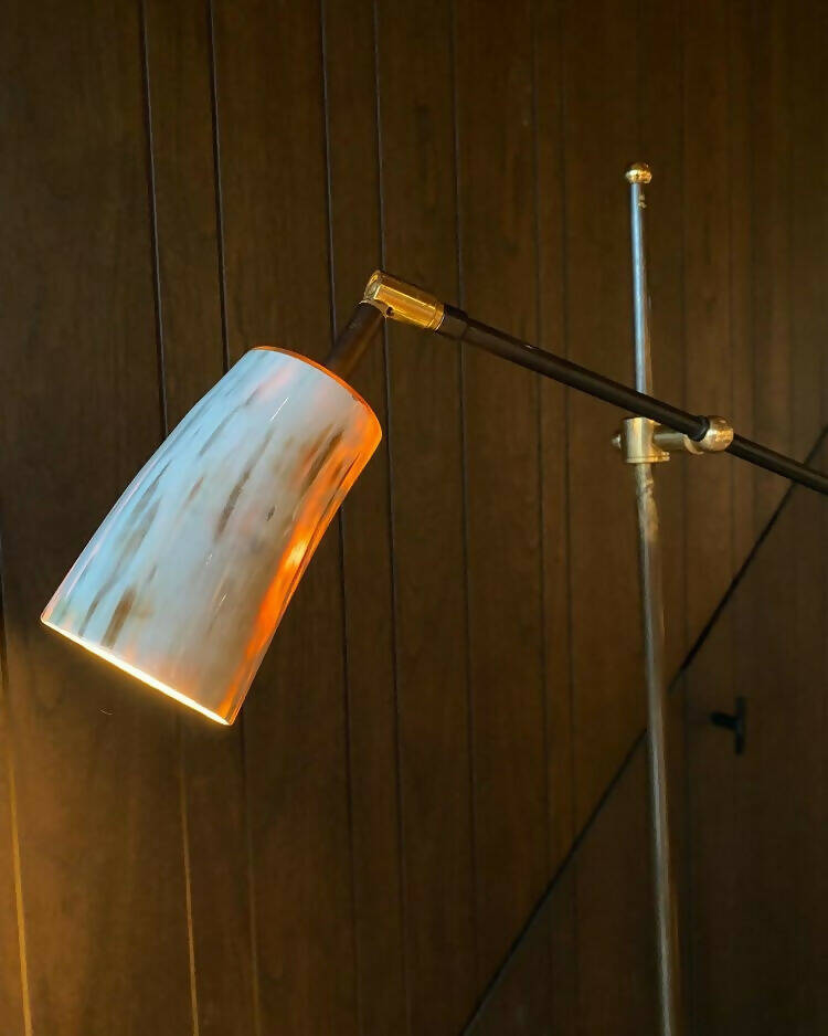 An floor lamp with a beige to black oyster-colored horn shade, mounted on a hand turned oak base with brass accents, placed against a wooden background,  available  to buy on the-salon.com. SALON curates the finest , unique, handmade pieces from the interior industry's best makers and brands. Shop luxury furniture, lighting, rugs, art, antiques and vintage pieces and accessories from SALON interior designed rooms.