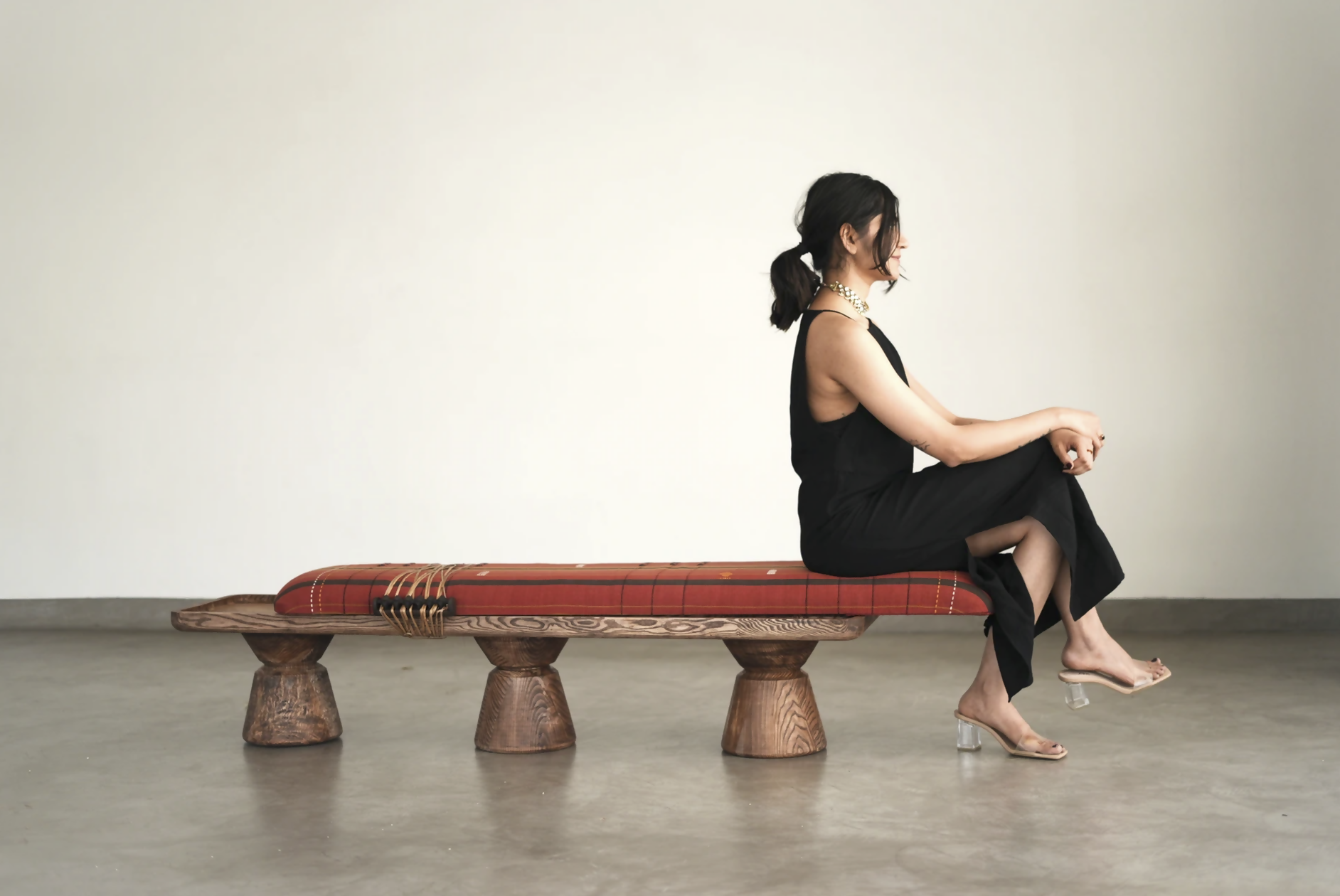 Woman sitting on a unique wooden bench with a plain background,  available  to buy on the-salon.com. SALON curates the finest , unique, handmade pieces from the interior industry's best makers and brands. Shop luxury furniture, lighting, rugs, art, antiques and vintage pieces and accessories from SALON interior designed rooms.